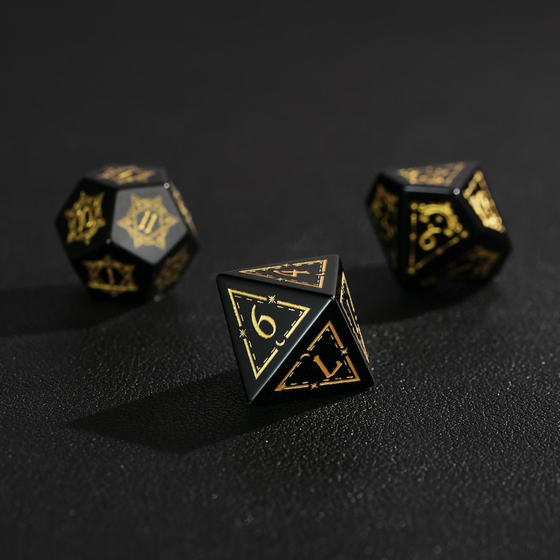 May include: Three black polyhedral dice with gold numbering and decorative accents. The dice are in various shapes, including a d20, d10, and d6. The dice are for tabletop games.