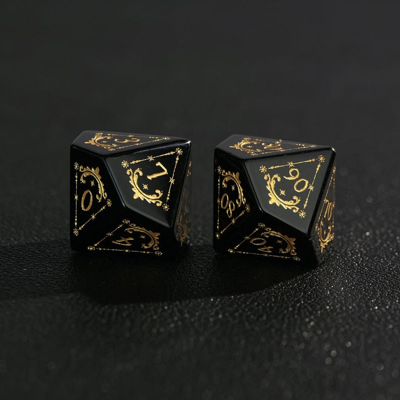 May include: Two black, multi-sided dice with gold-colored numbers and decorative flourishes. The dice are designed for role-playing games. The numbers are in a gold color and are set against a black background.