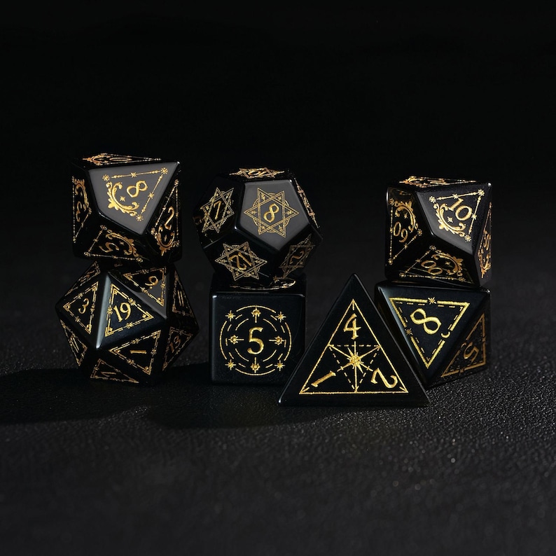 May include: A set of seven black polyhedral dice with gold-colored numbering and decorative accents. The dice include a D4, D6, D8, D10, D12, D20, and a percentile die, suitable for tabletop role-playing games.