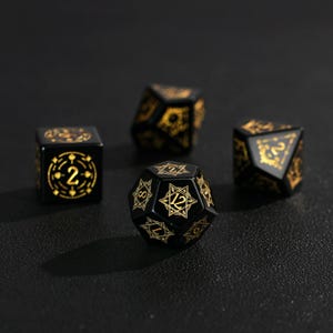May include: Four black polyhedral dice with gold-colored markings. The dice include a six-sided die, a twenty-sided die, and two other dice with different numbers of sides. The dice are for tabletop games.