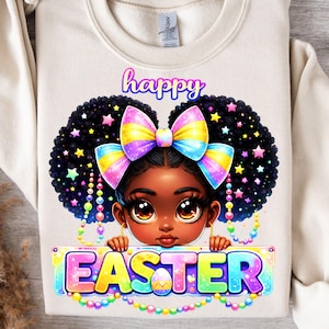 May include: A cream-colored sweatshirt featuring a cartoon illustration of a Black girl with a colorful bow and the words "Happy Easter." The girl has large brown eyes and is surrounded by stars. The word "EASTER" is written in colorful letters.