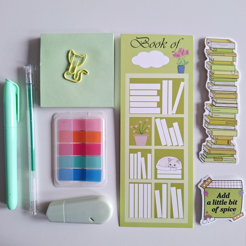 May include: A set of stationery supplies in green and pastel colors, including a notepad, a pen, a highlighter, a paper clip, a sticker, and a bookmark. The bookmark features a bookshelf with books and a cat. The sticker says "Add a little bit of spice".