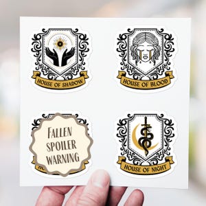 Puede incluir: Cuatro pegatinas con diseños de escudo. Una presenta un ojo y manos, con la etiqueta "House of Shadow". Otra muestra una cara llorando, con la etiqueta "House of Blood". Una tercera dice "Fallen Spoiler Warning". La última tiene una serpiente y una espada, con la etiqueta "House of Night".