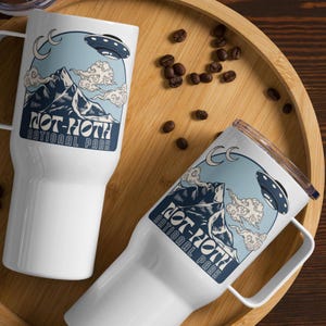 May include: Two white travel mugs with a blue and white design featuring a mountain range, clouds, and a UFO. The text on the mugs reads "Not-Hoth National Park".