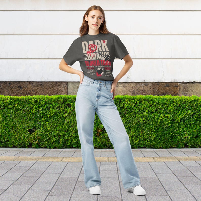 May include: A charcoal gray short-sleeve t-shirt featuring the text "DARK ROMANCE WORLD TOUR" in white and red, accompanied by a red rose graphic, a black heart, and a sword illustration, paired with light blue high-waisted denim jeans.
