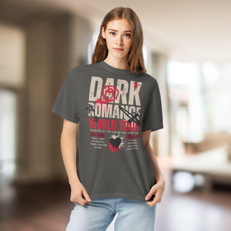 May include: A charcoal gray short-sleeve t-shirt featuring a graphic print that reads Dark Romance World Tour. The design includes red and white text, a black heart, a dagger, and star icons, with additional text listing various themes.