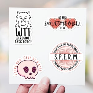 May include: A sheet of stickers with various designs. One sticker features a werewolf illustration with the text "WTF WEREWOLF TASK FORCE." Another says "in my DMATMOO-BIL era." Other stickers include a skull and the text "I LIKE YOU, GIVE US A KISS."