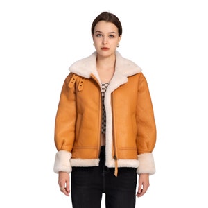 May include: A brown leather jacket with a white shearling collar and lining. The jacket has a zip fastening and two flap pockets.