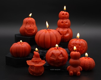 Peut inclure: Une collection de neuf bougies orange en forme de citrouille avec des visages sculptés. Les bougies sont allumées et dégagent une lueur chaleureuse.