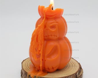Peut inclure: Bougie orange en forme de citrouille avec un visage sculpté, brûlant avec une flamme vive. La bougie est posée sur une base en tranche de bois, avec de la cire fondue qui coule sur le côté. Décoration festive d'Halloween.