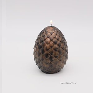 May include: A brown and black candle shaped like a dragon egg with a lit wick on top.