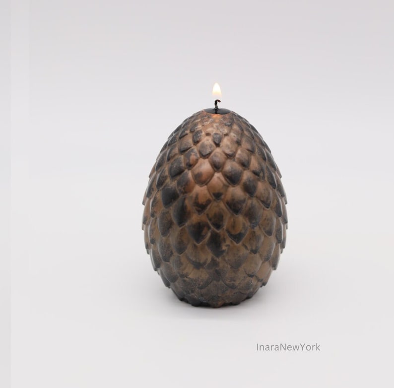 May include: A brown and black candle shaped like a dragon egg with a lit wick on top.