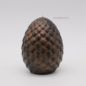 May include: A brown and black dragon egg-shaped candle with a white wick. The candle is textured to look like scales.