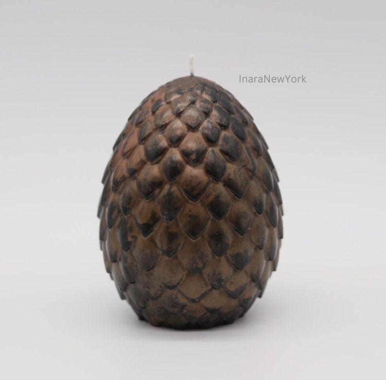 May include: A brown and black dragon egg-shaped candle with a white wick. The candle is textured to look like scales.