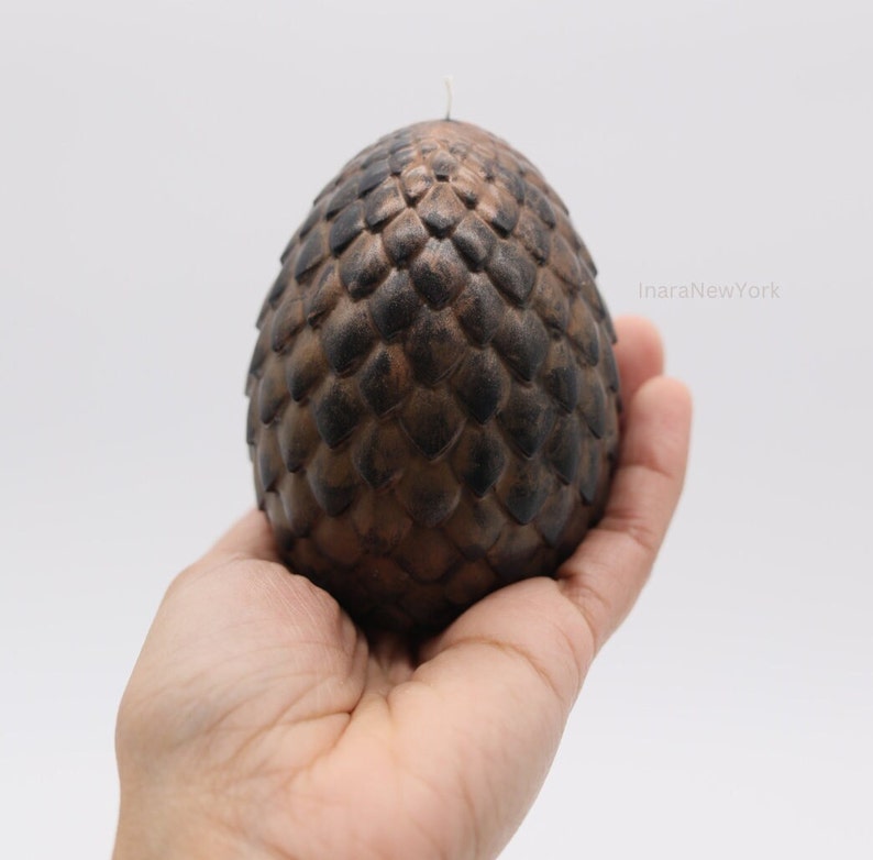 May include: A brown and black dragon egg candle with a textured surface. The candle is shaped like an egg and has a small wick on top.