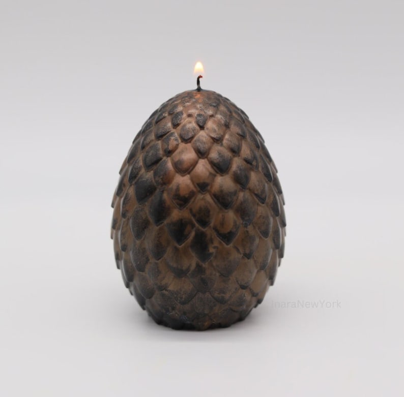 May include: A brown dragon egg-shaped candle with a lit wick on top. The candle is detailed with a textured, scaly design.