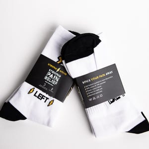 May include: A pair of white socks with black heels and toes. The socks have a yellow lightning bolt graphic and the text "Striking Pain Relief" and "Left" on the packaging. The socks are labeled "Sock Your Pain Away" and have a list of features on the packaging.