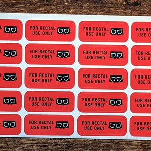 May include: A sheet of red rectangular stickers with black text and a black graphic of underwear. The text on each sticker reads "FOR RECTAL USE ONLY". The stickers are on a wooden surface.