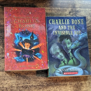 Pode incluir: Dois livros de capa dura, "Midnight for Charlie Bone" com capa vermelha e ilustração de um menino, e "Charlie Bone and the Invisible Boy" com capa azul e ilustração de um menino e uma serpente.