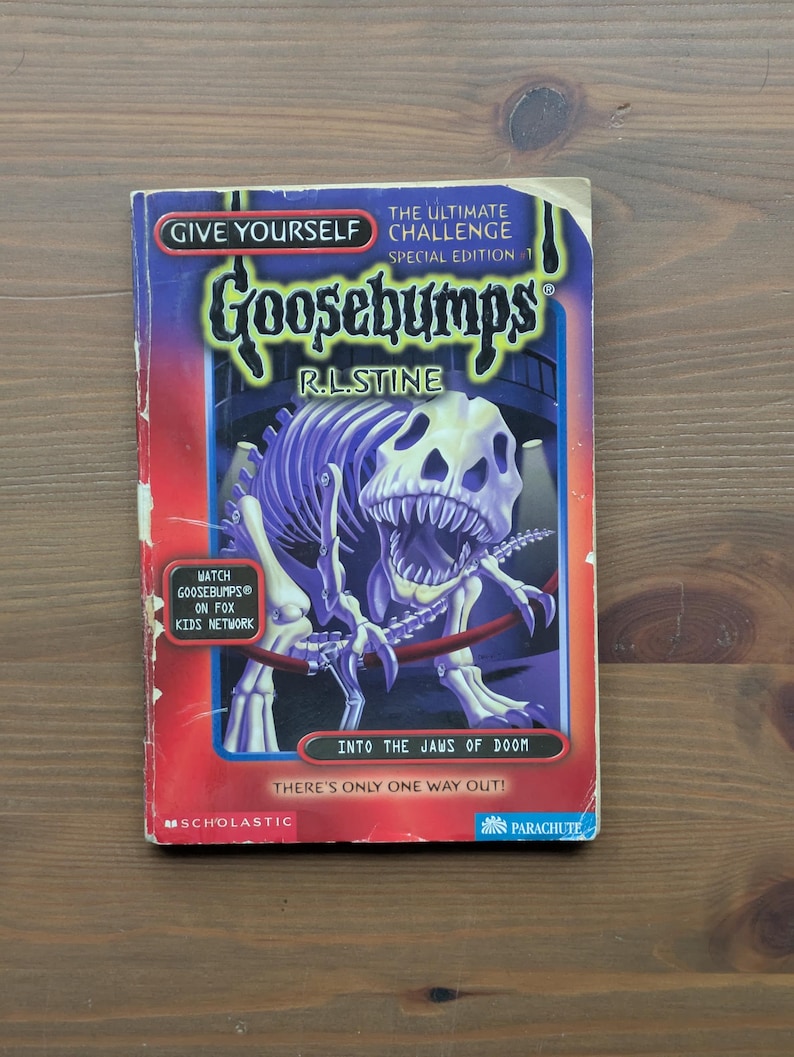 May include: A paperback book titled Give Yourself Goosebumps The Ultimate Challenge Special Edition 1 Into The Jaws Of Doom by R.L. Stine. The cover features a purple dinosaur skeleton illustration, red accents, and a Watch Goosebumps on Fox Kids Network badge.