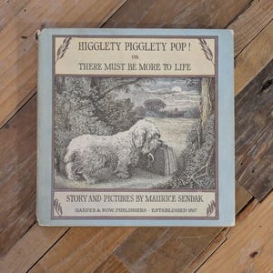 May include: A hardcover book titled Higglety Pigglety Pop! Or There Must Be More To Life, with story and pictures by Maurice Sendak. The cover features a light blue border and a black and white illustration of a shaggy dog standing by a suitcase.
