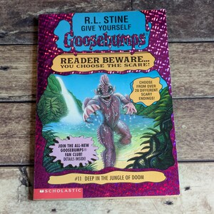 May include: A Give Yourself Goosebumps book titled Deep in the Jungle of Doom by R.L. Stine. The cover features a purple holographic border, a central illustration of a swamp creature in a jungle setting, and text promoting a fan club.