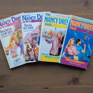 Puede incluir: Cuatro novelas de misterio vintage de Nancy Drew se exhiben sobre una superficie de madera. Las portadas de los libros presentan ilustraciones del personaje principal y títulos como "Secrets Can Kill" y "Crosscurrents". Los libros son de la serie Nancy Drew Files.