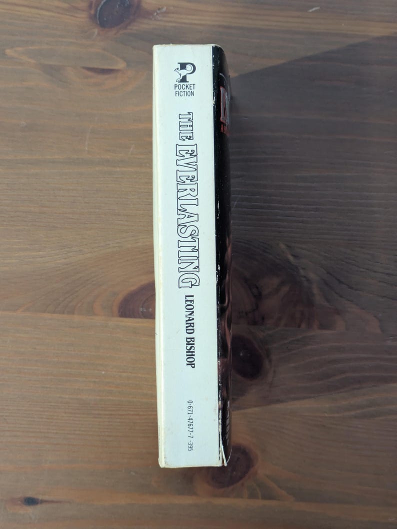 May include: A paperback book titled "The Everlasting" by Leonard Bishop. The spine is white with black text, featuring the Pocket Fiction logo. The book is set against a wooden background.