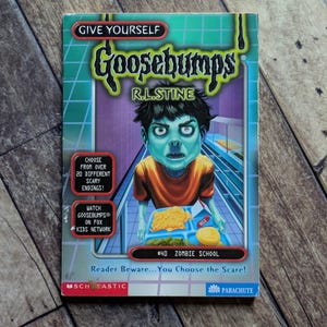May include: Give Yourself Goosebumps book number 40, Zombie School by R.L. Stine. The cover features a green-skinned zombie child in an orange shirt holding a cafeteria tray with food. Text includes Choose from over 20 different scary endings.