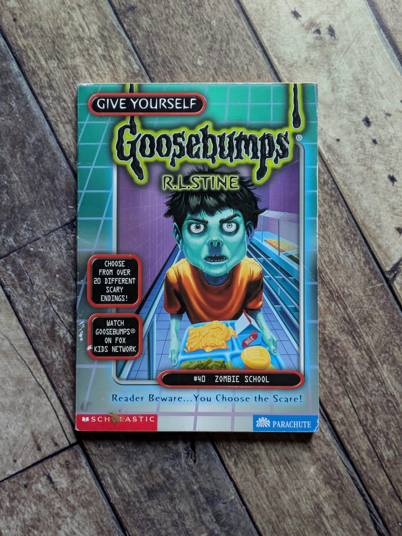May include: Give Yourself Goosebumps book number 40, Zombie School by R.L. Stine. The cover features a green-skinned zombie child in an orange shirt holding a cafeteria tray with food. Text includes Choose from over 20 different scary endings.