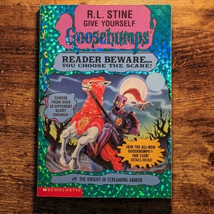 May include: A Goosebumps book titled The Knight in Screaming Armor by R.L. Stine with a holographic blue cover. The illustration features a knight in dark armor riding a red horse under a full moon. Text includes Reader Beware You Choose the Scare.