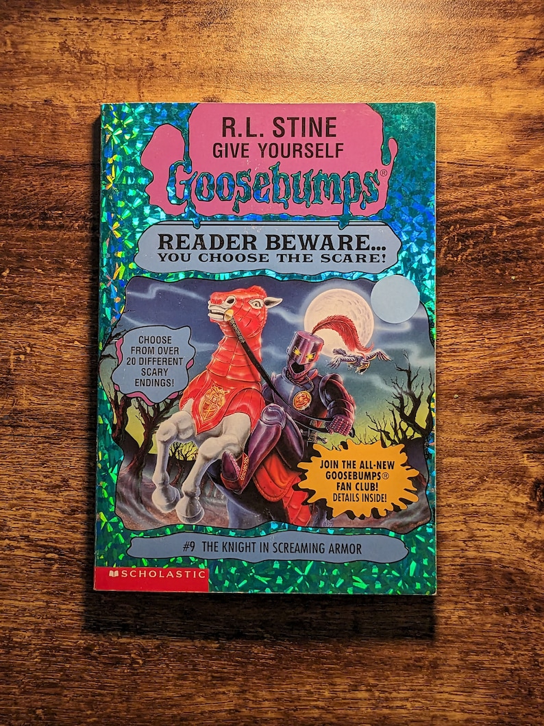 May include: A Goosebumps book titled The Knight in Screaming Armor by R.L. Stine with a holographic blue cover. The illustration features a knight in dark armor riding a red horse under a full moon. Text includes Reader Beware You Choose the Scare.