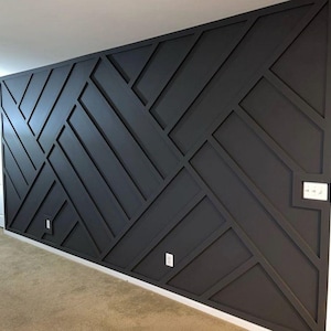 Puede incluir: Una pared negra con un patrón geométrico creado al agregar paneles de madera. Los paneles están dispuestos en un patrón repetitivo de líneas diagonales y rectángulos.