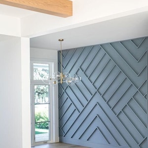 May include: A modern dining room with a light blue geometric wall panel and a gold chandelier with clear glass globes. The room has a white ceiling with wooden beams and hardwood floors.