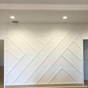 May include: A white wall with a geometric pattern created using white molding. The wall is painted white and has a subtle sheen. The molding creates a series of intersecting lines and shapes, forming a modern and stylish design.