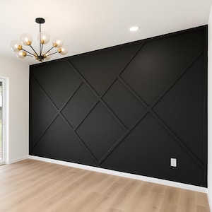 May include: A contemporary interior with a black feature wall showcasing a geometric pattern. The wall is set against light wood flooring and a white ceiling. A gold and glass chandelier hangs from the ceiling, lighting the room.