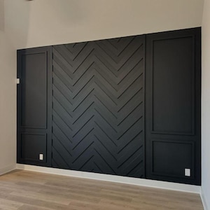 May include: A black accent wall with a herringbone pattern, framed by two black panels with a raised moulding design. The wall is in a room with light wood flooring.