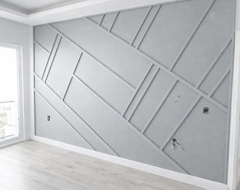 May include: A modern interior wall with a geometric design. The wall is painted in a light grey colour and features a pattern of rectangular and diagonal panels. The room has a window and light-coloured flooring.