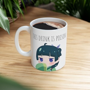 May include: White ceramic mug featuring the text "THIS DRINK IS POISON" and an anime-style illustration of a character with teal hair and purple eyes. The mug contains a dark liquid and has a white handle.