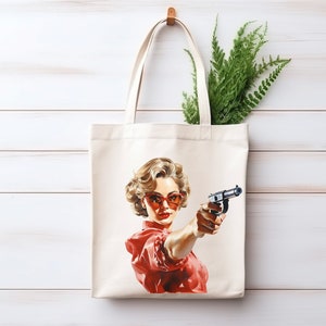 May include: A white tote bag with a red and white illustration of a woman wearing red sunglasses and holding a gun. The woman has blonde hair and is looking directly at the viewer.