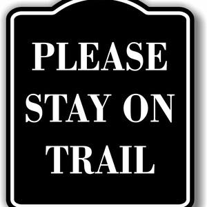 May include: Black and white sign with rounded edges and a white border. The sign reads "PLEASE STAY ON TRAIL".