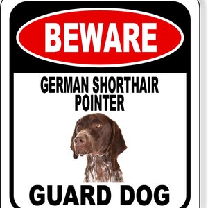 May include: A rectangular sign with a black border and white background. The top of the sign has a red oval with the word "BEWARE" in white. Below, it reads "GERMAN SHORTHAIR POINTER" and "GUARD DOG". A brown and white dog is in the center.