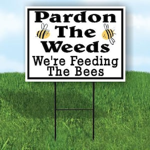 May include: A white sign with black text and cartoon bees reads "Pardon The Weeds We're Feeding The Bees".