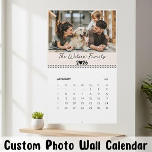 May include: A custom photo wall calendar featuring a family portrait at the top. The calendar displays the month of January 2026 with a spiral binding. The text "The Wilson Family" is above the calendar. The bottom of the calendar reads "Custom Photo Wall Calendar."