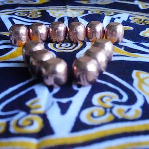 May include: A heart shape made of copper beads on a patterned fabric background. The beads are shiny and have a metallic finish.