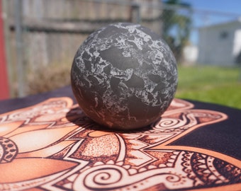 Puede incluir: Una esfera gris con una superficie texturizada se encuentra sobre una esterilla de yoga negra y naranja con un patrón de mandala.