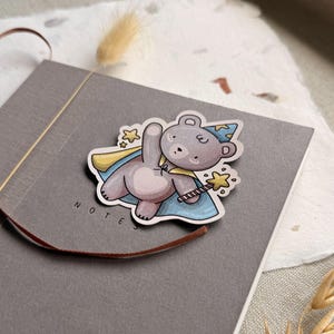 A charming cottagecore die-cut sticker featuring a teddy bear dressed as a wizard, complete with a pointed hat, flowing cape, and a magic wand sparkling with stars. Perfect for adding a touch of whimsy to laptops, water bottles, and journals.