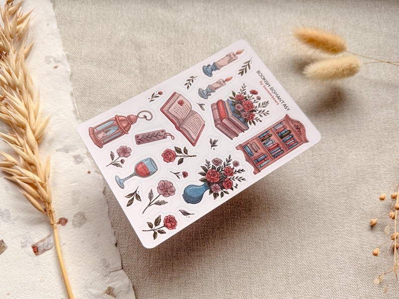 Bookish Romantasy cottagecore sticker sheet featuring pile of books with flowers, open book, lantern, vase with flowers, shelf full of books, single floral stickers, and glass of wine, with dreamy book lover aesthetic.
