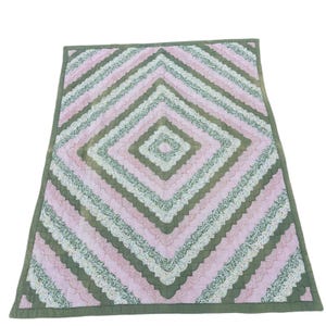 May include: A handmade quilt with a diamond pattern. The quilt features alternating rows of pink, green, and floral fabric. The edges are finished with a green border. The quilt is likely made of cotton and is suitable for a bed or as a decorative throw.
