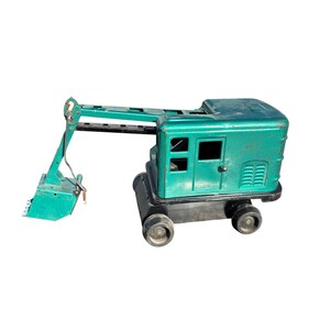 May include: Vintage toy excavator in teal green with black wheels and base. The metal toy has a detailed boom and bucket, and a cabin with window details. A classic construction toy.